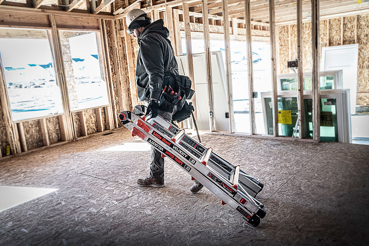 A worker carrying a ladder at a construction site