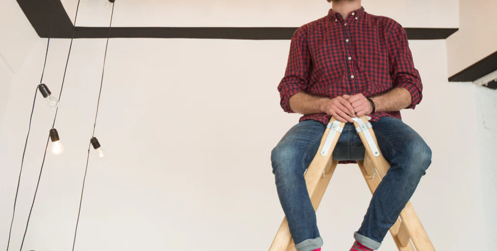 a guy sitting on a ladder trying to fix indoor lamp on house ceiling