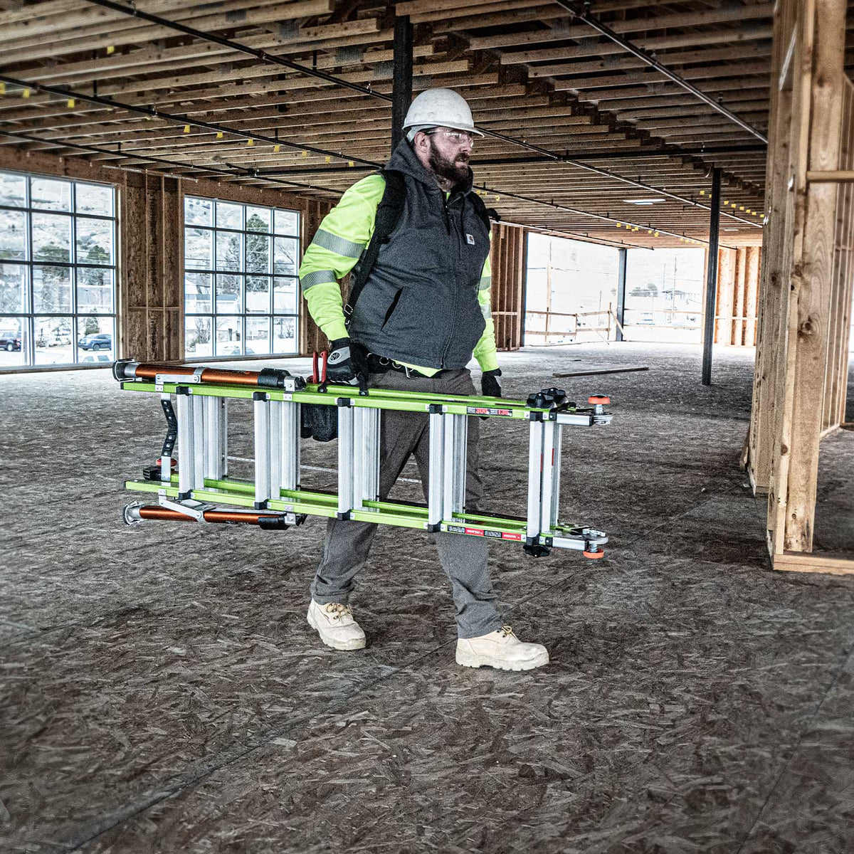 Construction worker in safety gear carrying a Conquest 2.0 across a busy construction site.