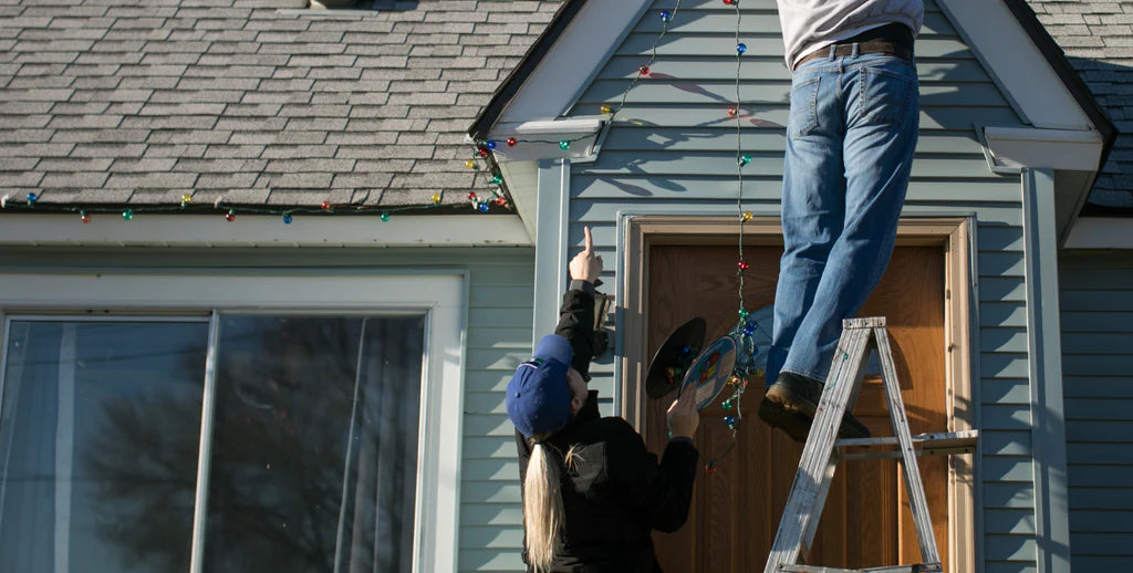 a man on a ladder setting up Christmas lights on a roof 