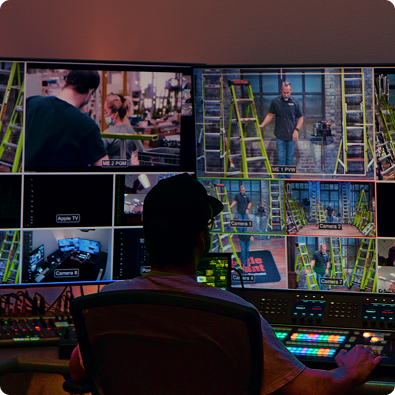 Person working at a control room with multiple monitors displaying video feeds.