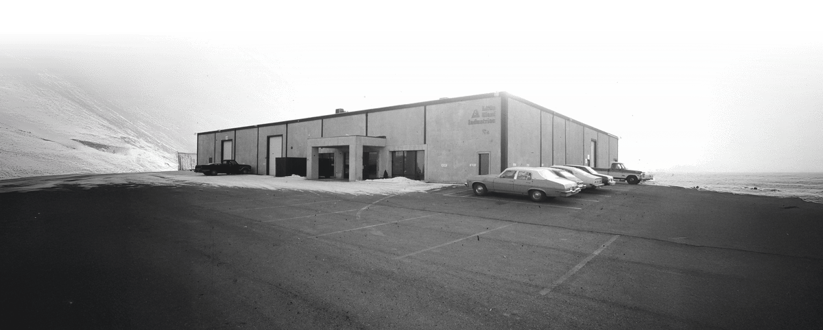 Large industrial building with a car parked in front, black and white photo.